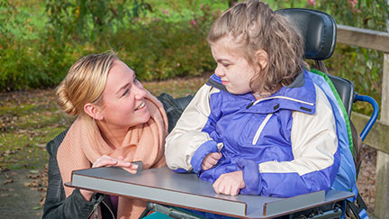 blonde woman smiling at girl in wheelchair in a park